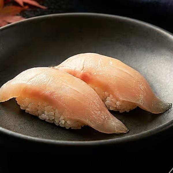 Two pieces of delicate nigiri sushi with light pink fish on white rice, served on a dark plate.