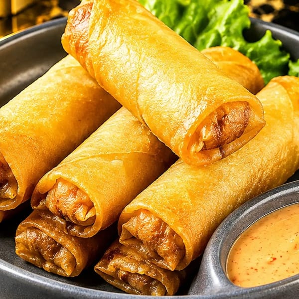 Golden-fried spring rolls with lettuce and a side of dipping sauce on a dark plate.